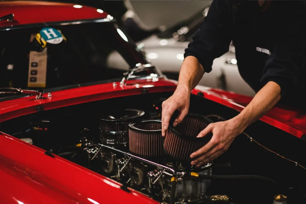 Mechanic installing performance air filter on classic red car engine at auto repair shop