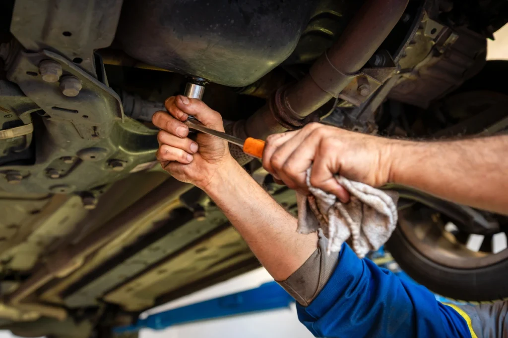 Mechanic working under car with wrench and screwdriver performing vehicle undercarriage repair at auto shop